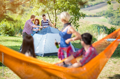 Young people on camping setting tent in forest