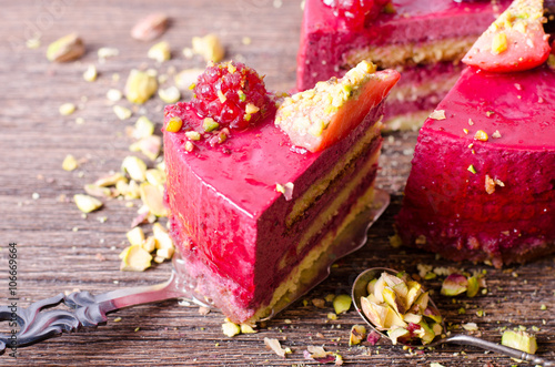 Piece of delicious raspberry cake with fresh strawberries, raspberries, blueberry, currants and pistachios on shovel, wooden background. Free space for your text. photo