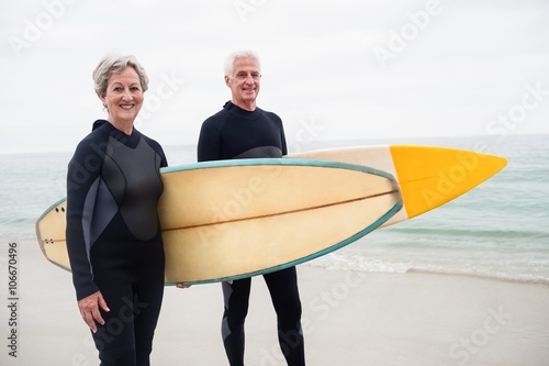 Senior couple with surfboard standing on the beach