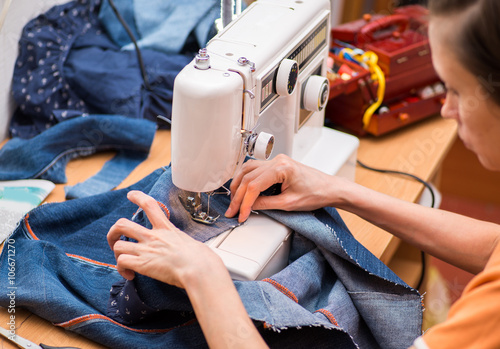 young woman sews on the sewing machine denim