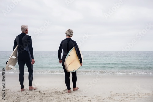 Canvastavla Rear view senior couple in wetsuit holding a surfboard