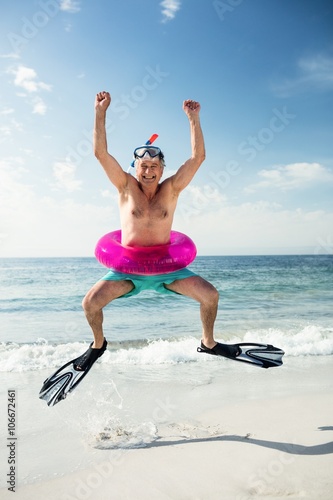 Portrait of senior man in inflatable ring and flippers jumping on beach on a sunny day