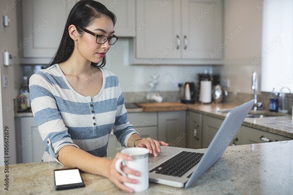 Young woman using a laptop in the kitchen Young woman using a laptop in the kitchen