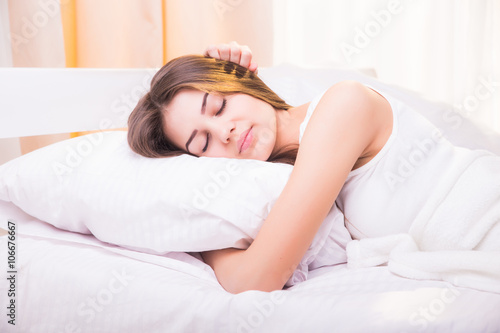 A sleeping woman is lying in bed with her head on the pillow and hands under it.