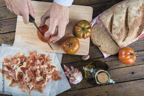 Cocinero cortando el tomate y el pan para preparar tostas tradicionales de jamón con pan tumaca photo