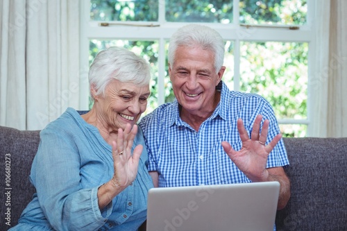 Smiling senior couple waving hand while using laptop 