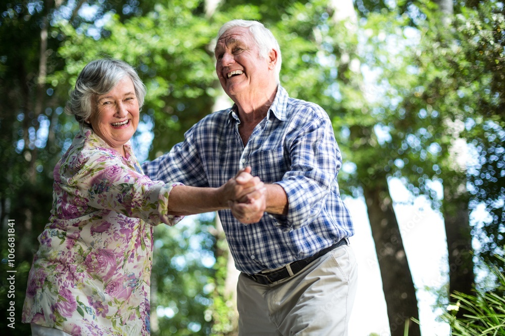 Happy senior woman dancing with husband against trees Happy senior woman dancing with husband against trees