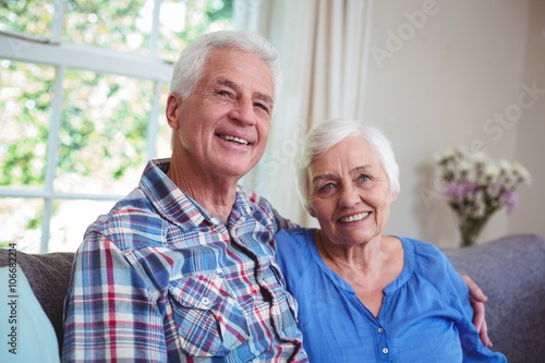 Senior couple sitting with arms around on sofa