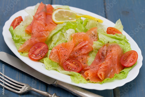 salad with smoked salmon on white dish on blue background
