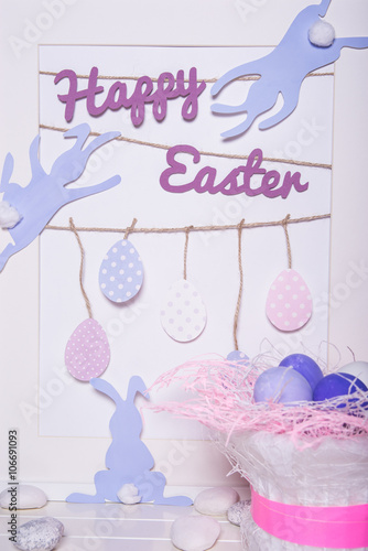 Happy Easter! Easter Bunny to reach for the inscription Happy Easter on white background. On a rope hanging Easter eggs.