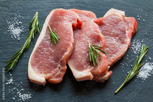 Foto Raw pork steaks with rosemary on black stone background.