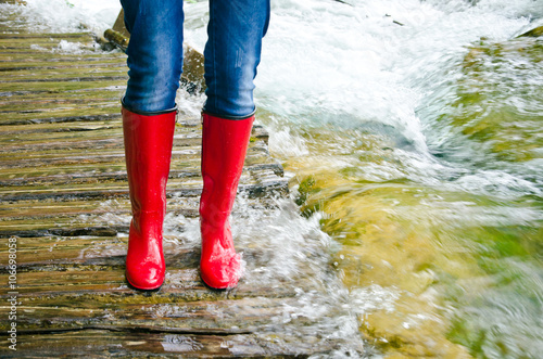 red rubber boots in water on wooden bridge, river overflowed its banks. 