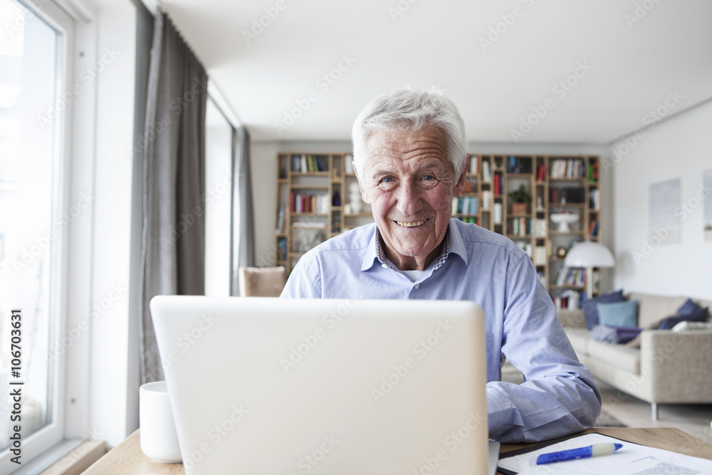 Portrait of senior man sitting at table in the living room with laptop Portrait of senior man sitting at table in the living room with laptop
