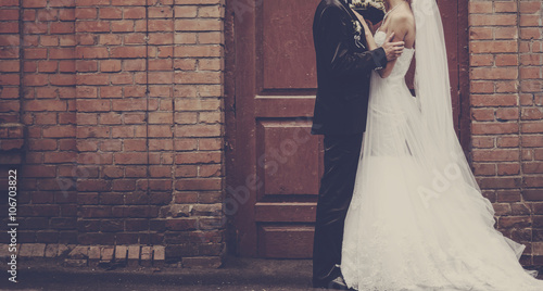 Newlyweds embracing next to red brick wall. photo