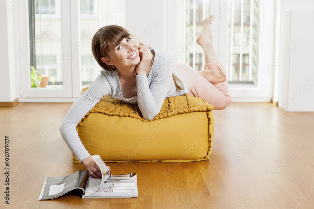 Relaxed woman reading magazine on ottoman at home Relaxed woman reading magazine on ottoman at home