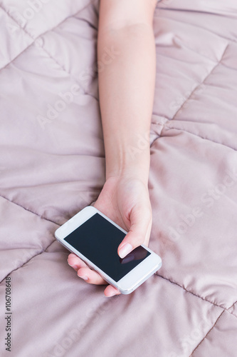 Woman hand with mobile phone sleeping on bed.