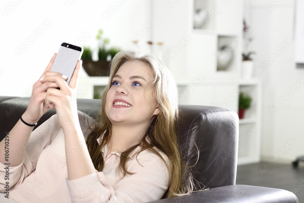 Jugendliche lachend mit Handy auf Sofa im Wohnzimmer