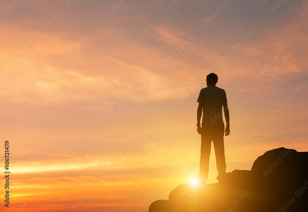 Landscape with silhouette of a standing man on the background of colorful yellow sky on the rock at sunset.
