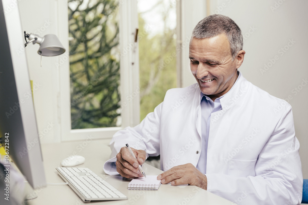Smiling doctor sitting at desk with computer Smiling doctor sitting at desk with computer