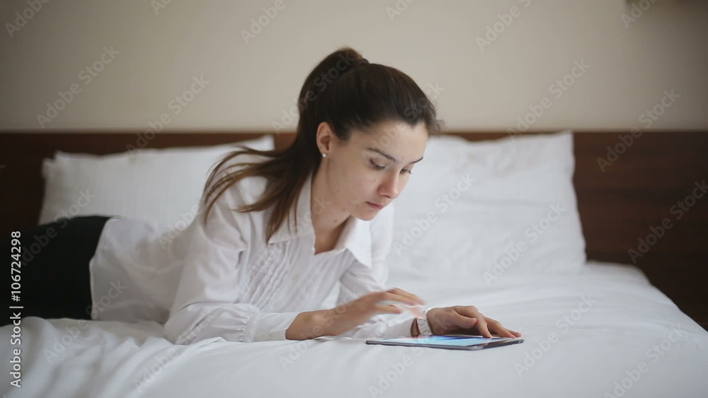 Woman lies on the bed scrolling through her tablet Woman lies on the bed scrolling through her tablet