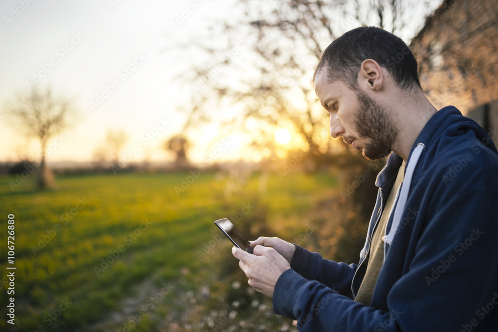 Man typing on a smartphone in a green field at sunset Man typing on a smartphone in a green field at sunset