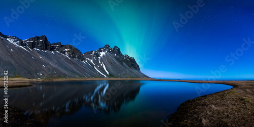 Panoramic of Northern lights and mountains behind a lake
