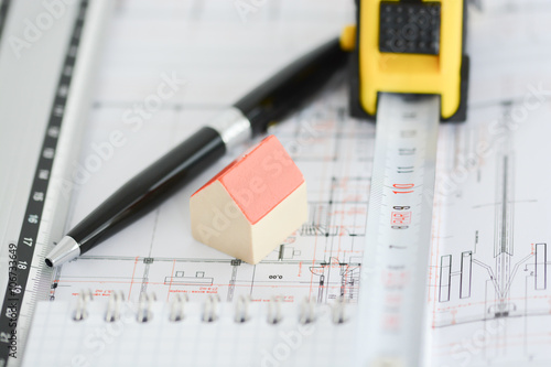 Architecture plans of a building with Small model house on top of blueprints, pen, ruler and notebook 