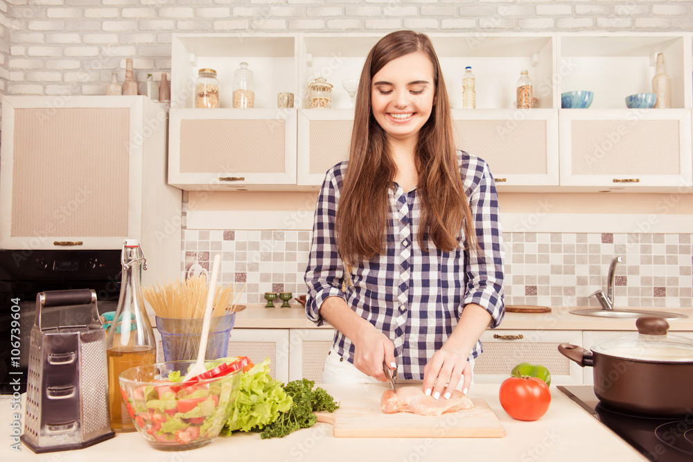 Young happy housewife making breakfast and cutting meat