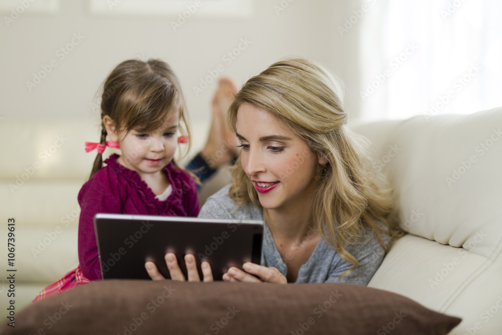 Mother and her little daughter together on couch in the living room looking at digital tablet Mother and her little daughter together on couch in the living room looking at digital tablet
