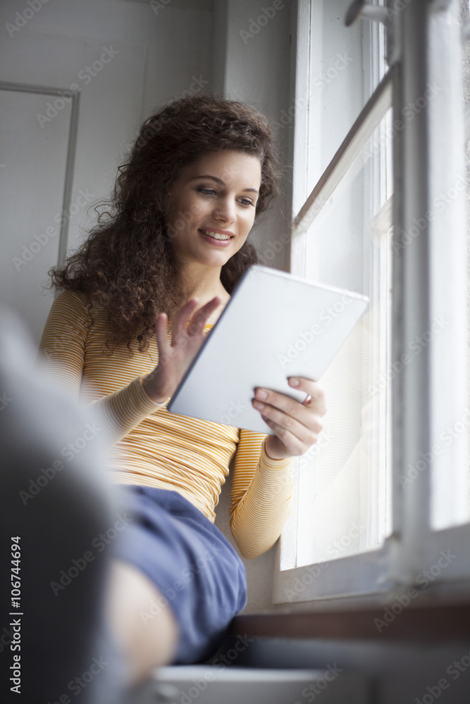 Smiling young woman using digital tablet at the window Smiling young woman using digital tablet at the window