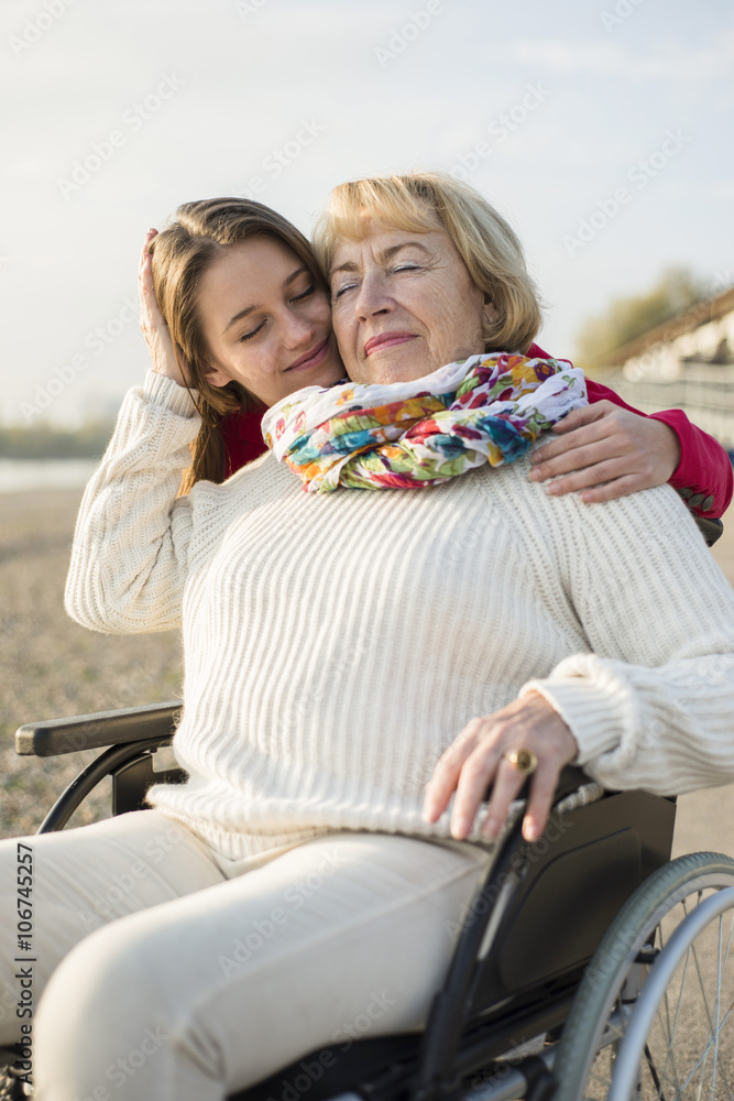 Young woman head to head with her grandmother sitting in wheelchair Young woman head to head with her grandmother sitting in wheelchair