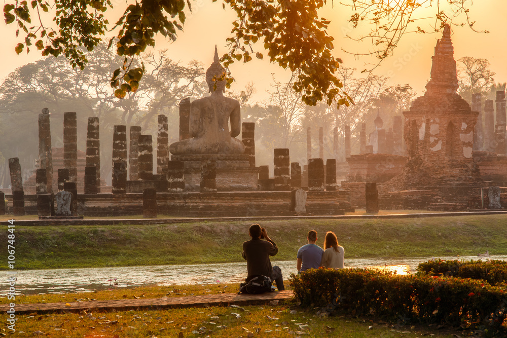 Obraz premium Japanese Man take a photo european traveller in sunrise time at Sukhothai historical park, the old town of Thailand in 800 years ago