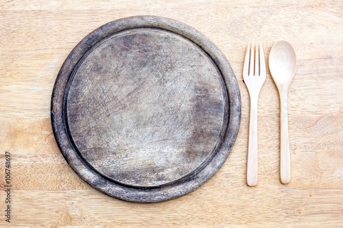 old round wooden cutting board with spoon and fork on a table ba