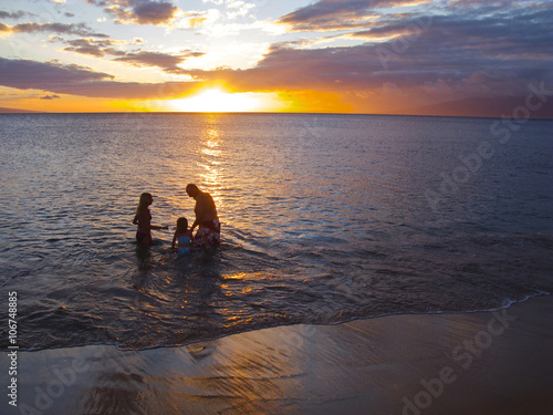 Fototapeta Naklejka Na Ścianę i Meble -  A family enjoys the surf on a Maui beach at sunset.