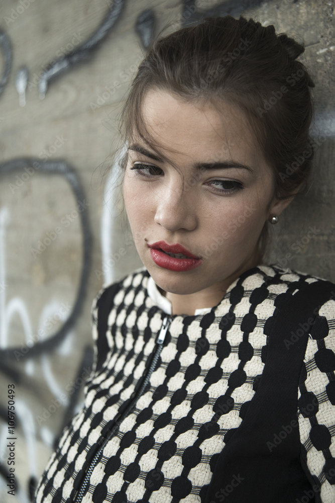 Portrait of sad young woman with red lips in front of wall with graffiti