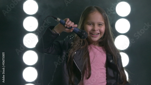 Young Asian American girl dancing with microphone with smoke and stagelight in background. photo