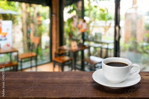 A Cup of coffee on a rustic wooden table with coffee shop blurred background.