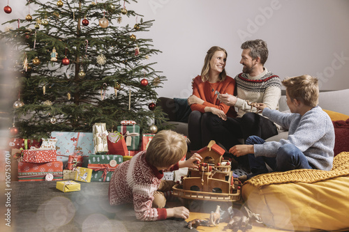 Family of four unwrapping Christmas gifts and playing with Noah's Ark