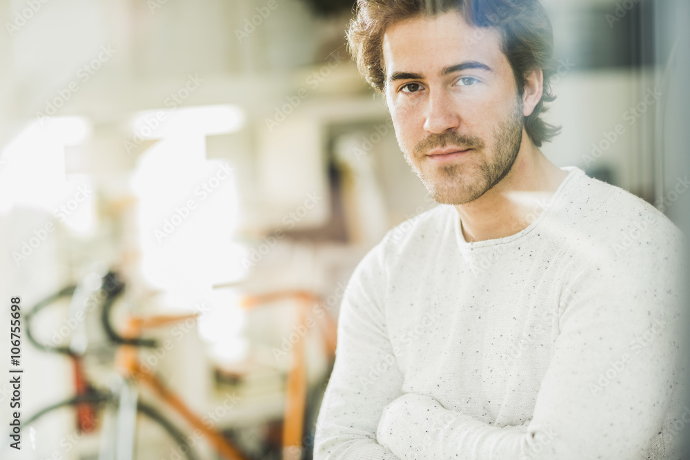 Portrait of young man with arms crossed looking through windowpane