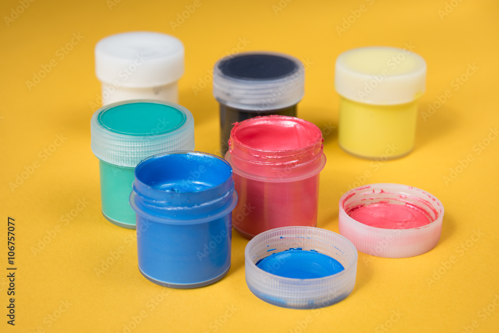 Opened bottles of watercolor paint on a yellow paper Opened bottles of watercolor paint on a yellow paper