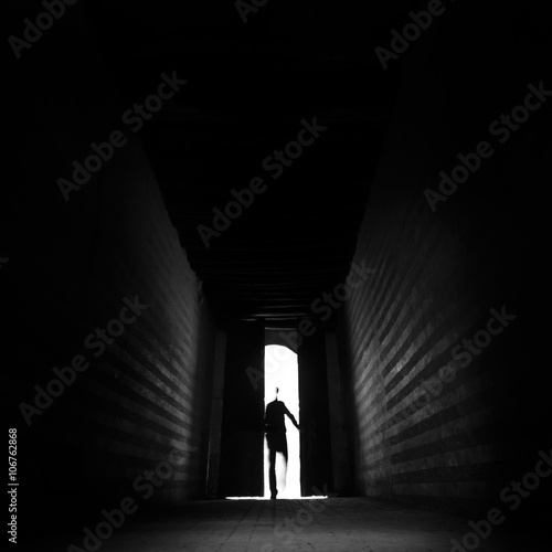 Obraz na plátně Person's silhouette entering trough doorway to dark backlit hall
