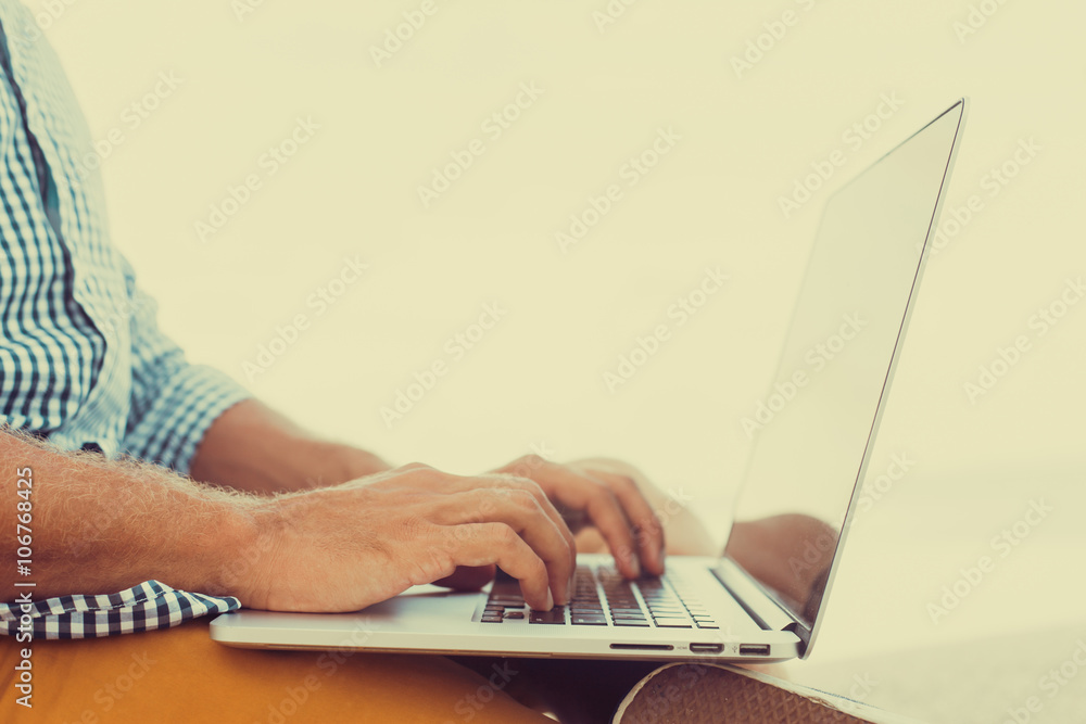 Young man working on laptop while sitting on the beach on the pier, sending mail, mounts, video editing and photography,working abroad,freelance working,typing online,social networks,periscope,wi- Young man working on laptop while sitting on the beach on the pier, sending mail, mounts, video editing and photography,working abroad,freelance working,typing online,social networks,periscope,wi-