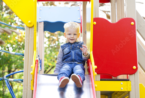 Blonde little boy sits on a childrens slide at the playground © Andrey_Arkusha