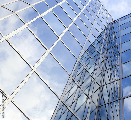 glass office facade reflects clouds and blue sky