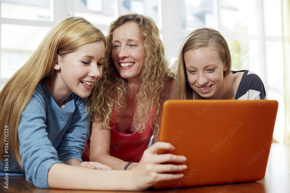Mother and her two daughters lying on wooden floor at home using laptop Mother and her two daughters lying on wooden floor at home using laptop