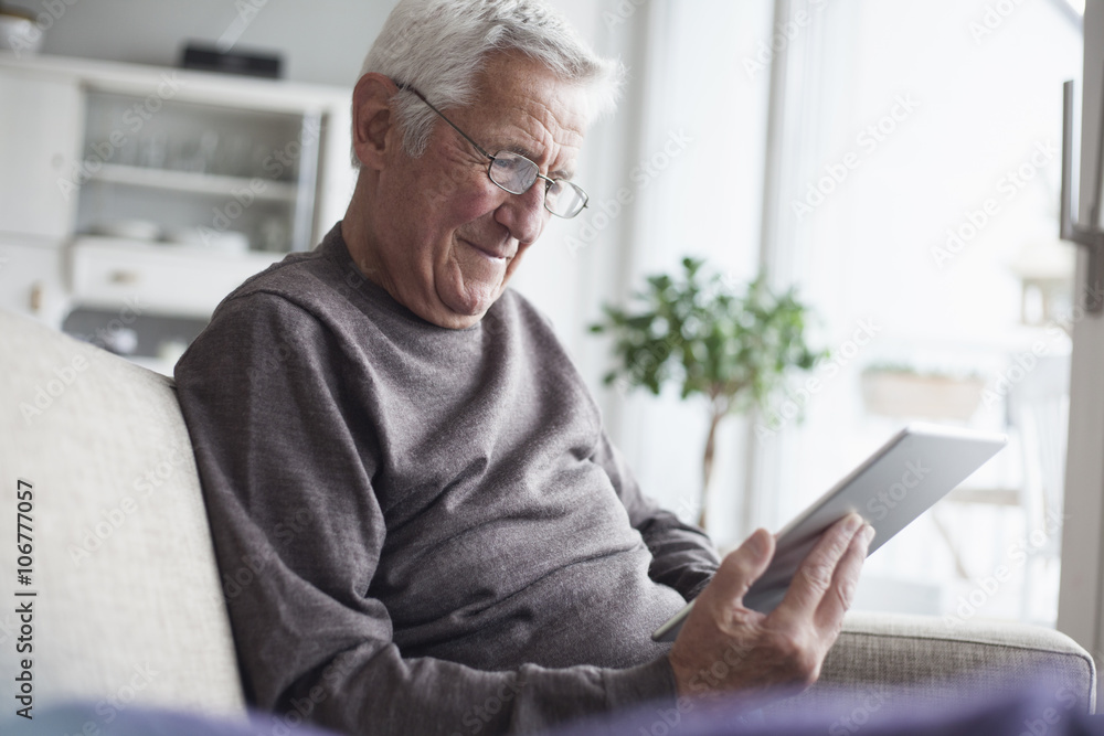 Portrait of senior man sitting on couch at home using digital tablet Portrait of senior man sitting on couch at home using digital tablet