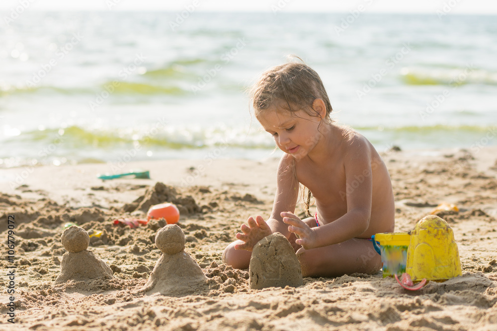 The child sits on the sandy beach of the reservoir and enthusiasm molds of sand cakes The child sits on the sandy beach of the reservoir and enthusiasm molds of sand cakes