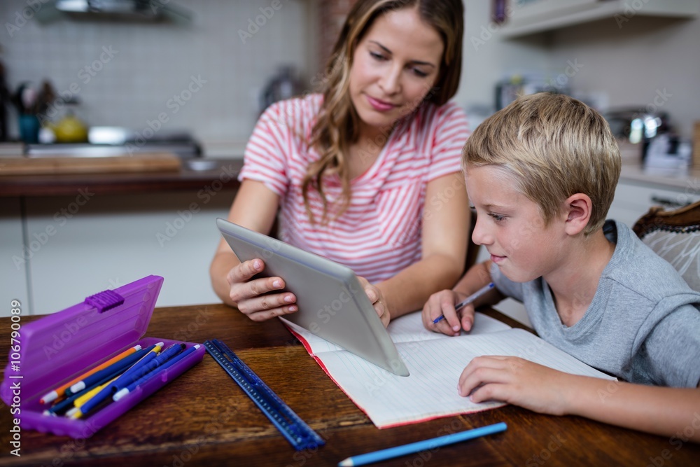 Fototapeta premium Mother using tablet while helping son with his homework
