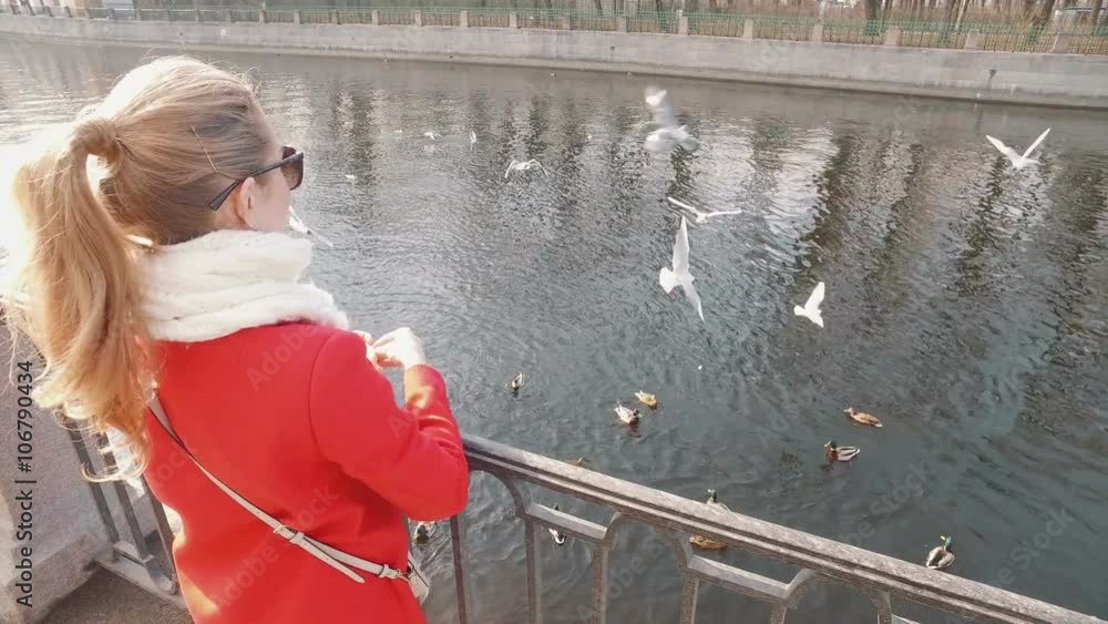 Young blond woman feed ducks in on a sunny spring day