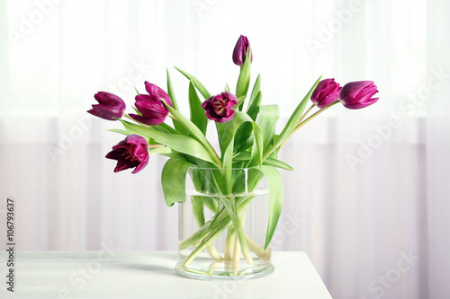 A bouquet of violet tulips in a vase on white table.